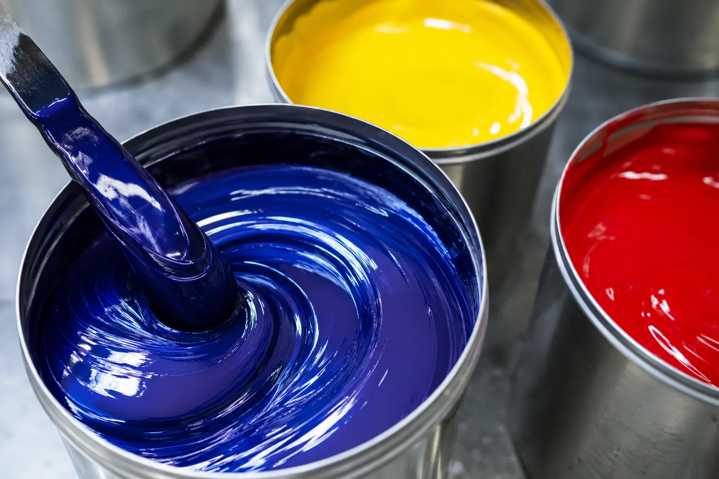 Espátula mezclando tinta azul en un bote junto a botes de tinta amarilla y roja